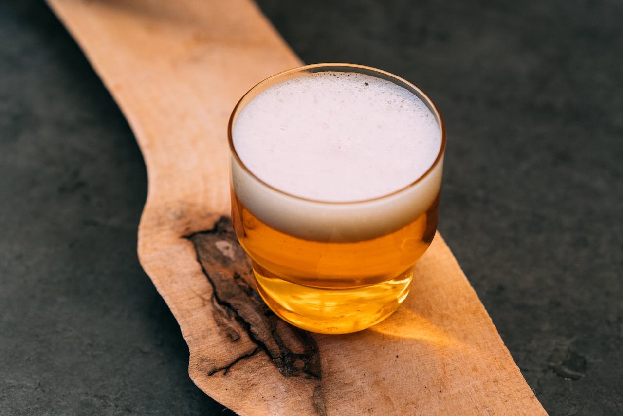 A small glass of craft beer with foam, placed on a rustic wood surface, shot in cozy warm tones.