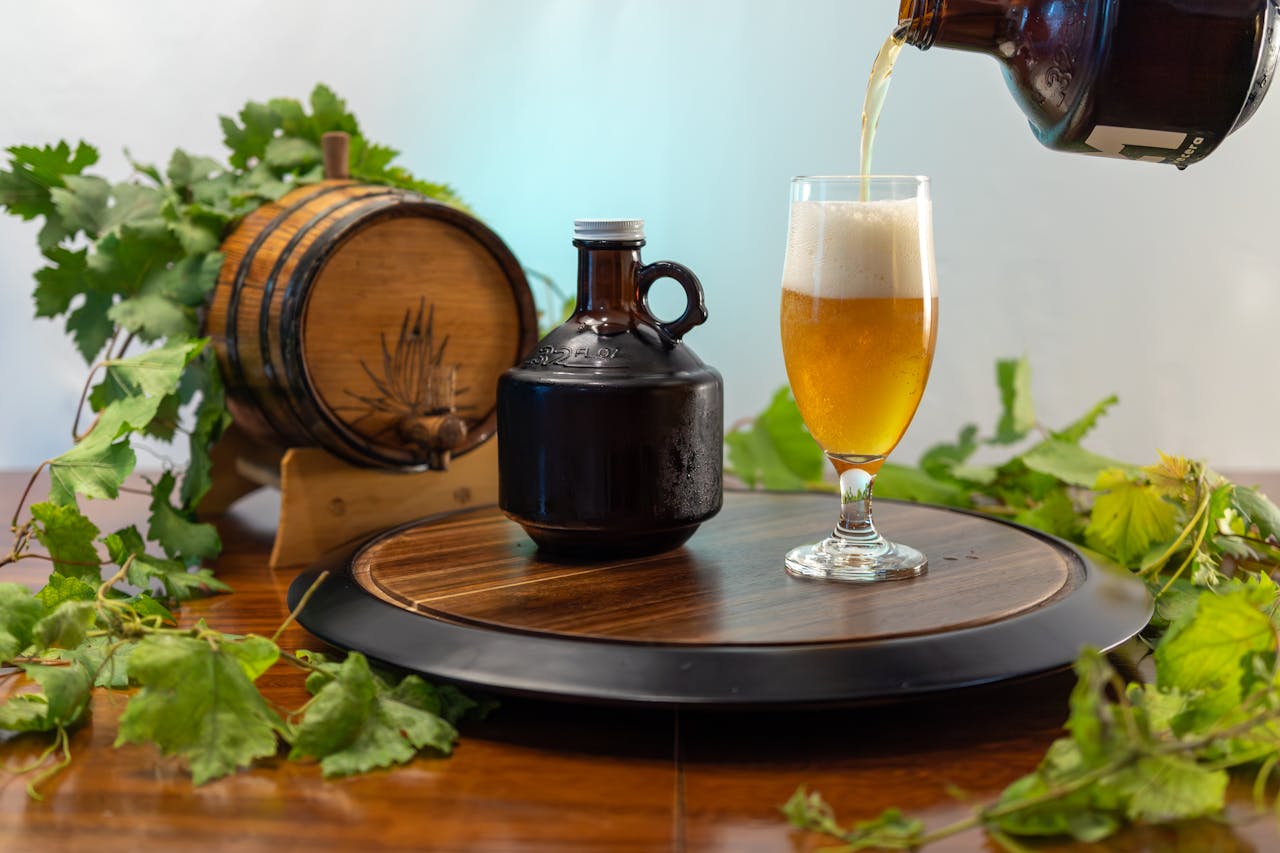 Craft beer being poured into a glass with a wooden barrel and vine leaves in the background for a rustic look.